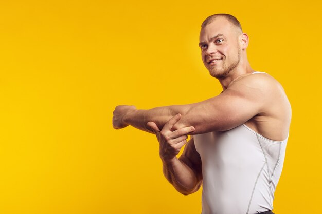 격리 된 노란색 벽 위에 서있는 흰 셔츠에 근육 질의 남자의 초상화