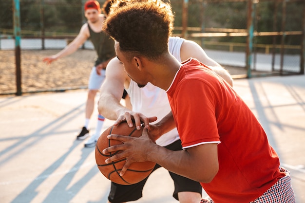 夏の晴れた日の間に、屋外の遊び場でバスケットボールをしている筋肉のスポーティな男の子の肖像画