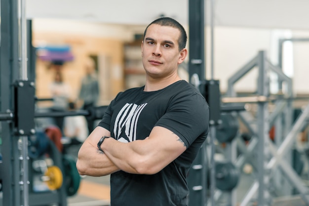 Portrait of muscular sporty man with folded hands in the gym