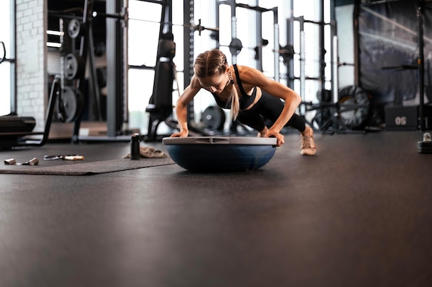 Portrait of a muscular woman on a plank position with bosu at gym