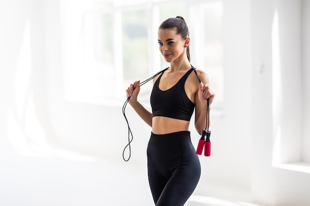 Photo portrait of muscular young woman exercising with jumping rope on white background