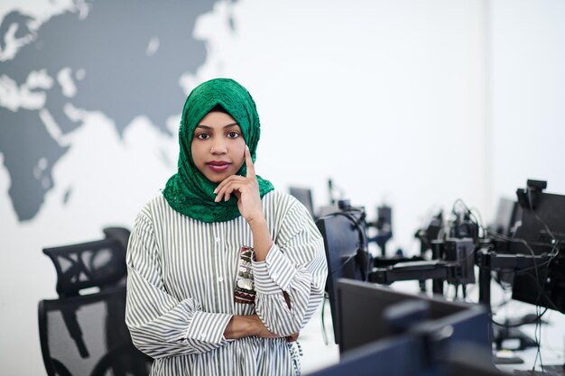 Portrait of muslim african female software developer with green hijab standing at modern open plan startup office