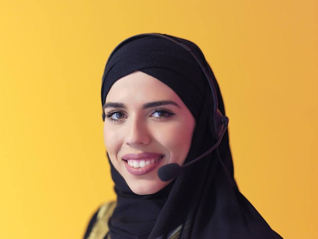 Photo portrait of muslim female with hijab scarf customer representative business woman with phone headset helping and supporting online with customer in modern call centre isolated on yellow background