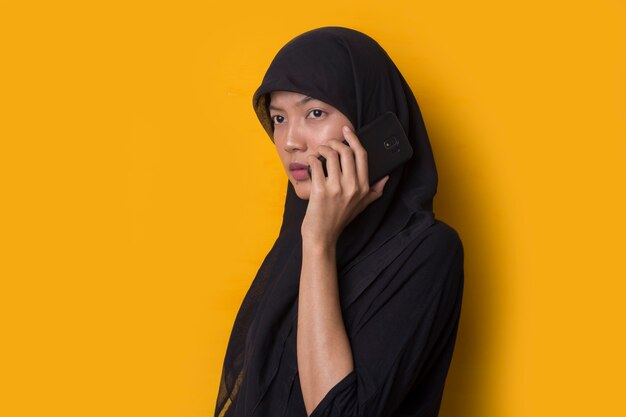 Portrait of muslim girl using a smartphone on yellow background