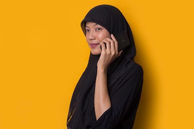 Portrait of muslim girl using a smartphone on yellow background