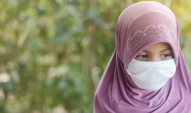 Portrait of Muslim kid girl with hijab wearing mask. Covid-19 or Coronavirus concept.