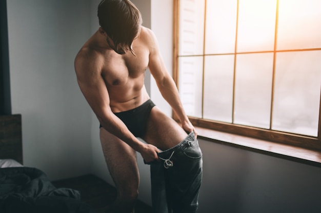 Portrait of naked bearded dark-hair handsome man is dressing cloth at home