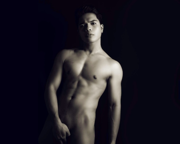 Photo portrait of naked young man standing against black background