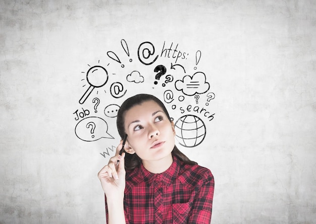 Photo portrait of a nerdy girl wearing a checkered shirt and sitting in a room with a black internet search sketch drawn on a concrete wall behind her.