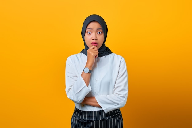 Portrait of nervous beautiful Asian woman looks worried and hand on lips on yellow background