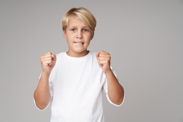 Portrait of nervous blonde boy fan posing isolated over grey wall showing hopeful gesture.