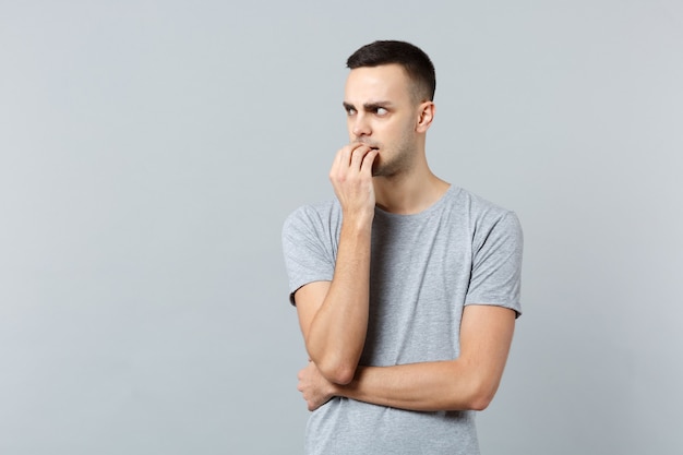 Portrait of nervous young man in casual clothes gnawing nails looking aside 