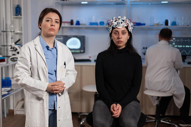 Ritratto di medico neurologo in piedi accanto a paziente donna con auricolare medico eeg durante l'esperimento di neuroscienze in laboratorio medico. team di ricercatori che analizzano l'evoluzione dell'attività cerebrale