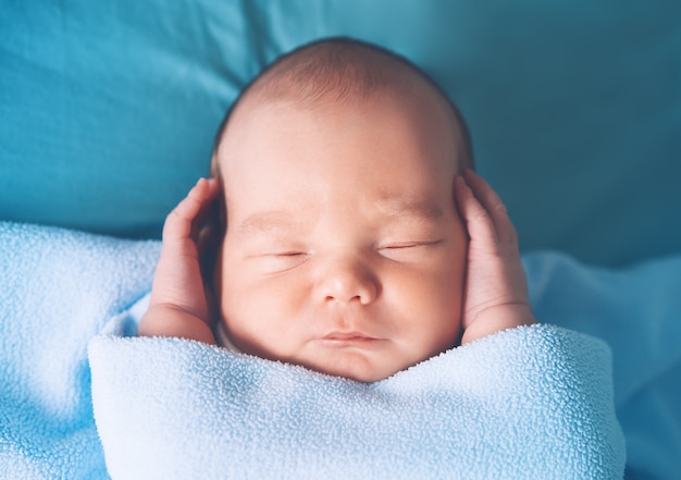 布の背景のベビーベッドで安らかに眠っている1週齢の生まれたばかりの子供の男の子の肖像画