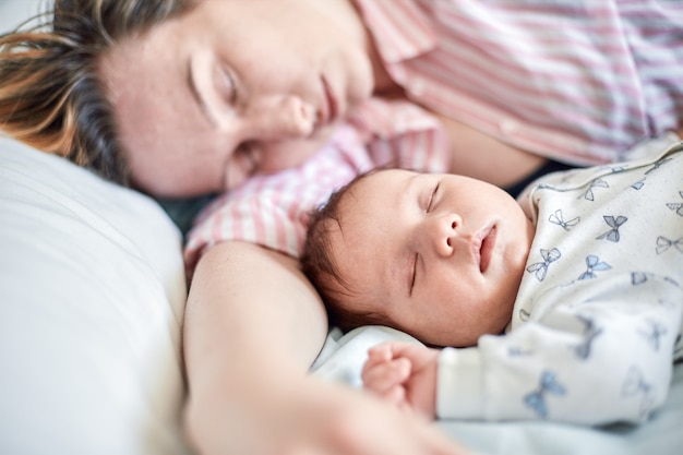 Photo portrait of newborn baby and mother sleeping on bed, resting together