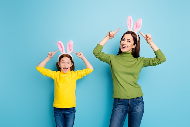 Portrait of nice attractive lovely charming pretty cheerful cheery girls wearing demonstrating rabbit ears having fun isolated over bright vivid shine vibrant blue color