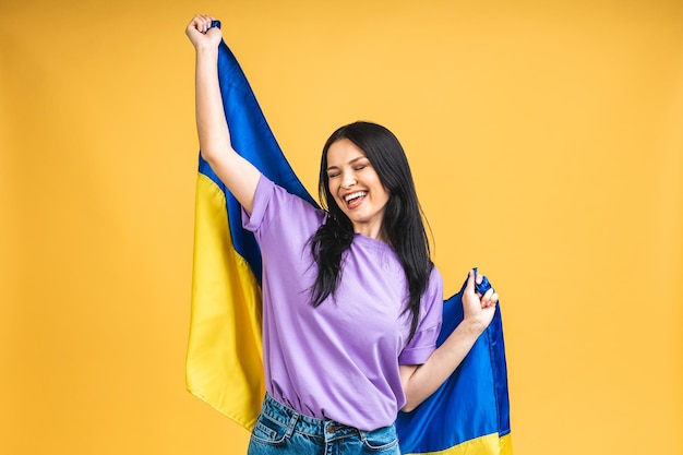 노란색 파스텔 색상 배경에서 고립되어 즐거운 시간을 보내는 우크라이나 국기를 손에 들고 있는 멋지고 사랑스러운 쾌활한 여성의 초상화