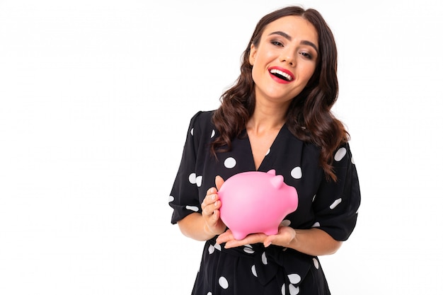 Portrait of nice caucasian girl holds a money box and thinks on white