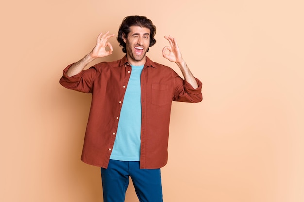 Portrait of nice excited cheerful guy showing double ok-sign winking isolated over beige pastel color background