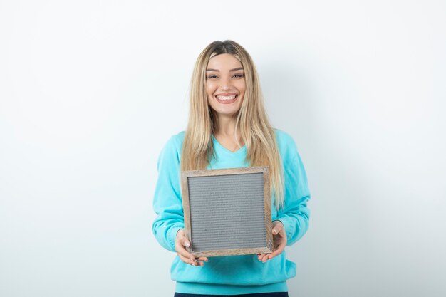 Portrait of nice-looking lady holding frame against white wall