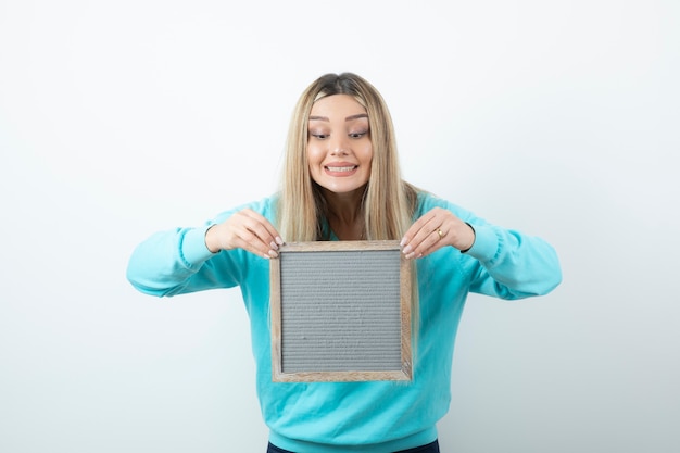 Portrait of nice-looking lady holding frame against white wall