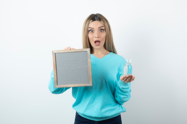 Portrait of nice-looking lady holding in hands frame and glass pitcher