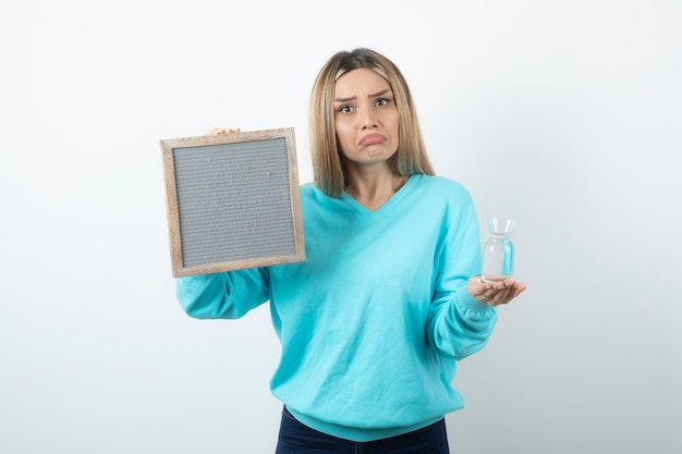 Portrait of nice-looking lady holding in hands frame and glass pitcher