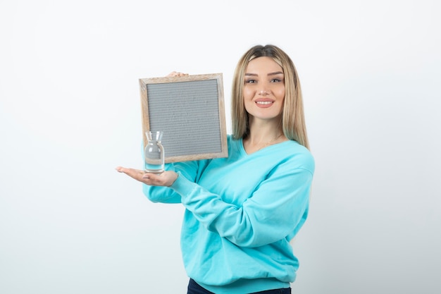 Portrait of nice-looking lady holding in hands frame and glass pitcher