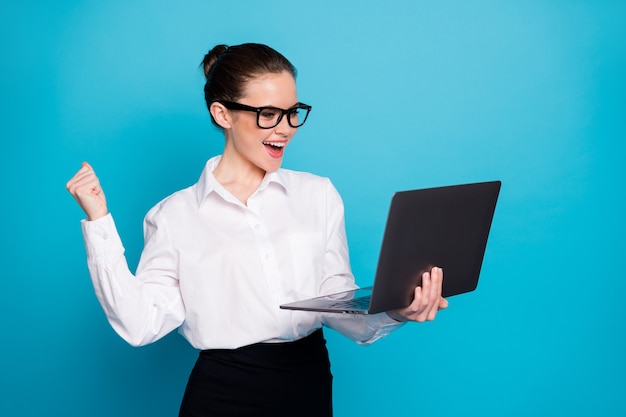 Ritratto di una ragazza esperta e allegra simpatica che tiene in mano un laptop che celebra isolato su uno sfondo di colore blu brillante