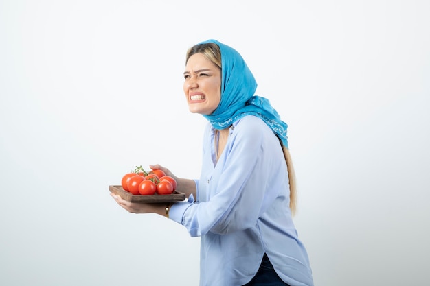 Portrait of nice woman in blue shawl holding wooden board of red tomatoes