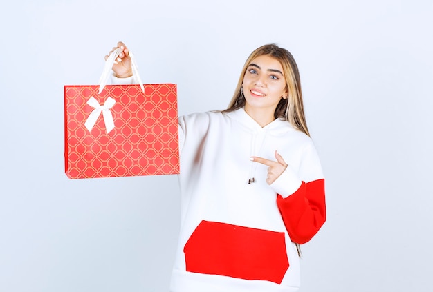 Portrait of nice woman model standing and pointing at gift bag