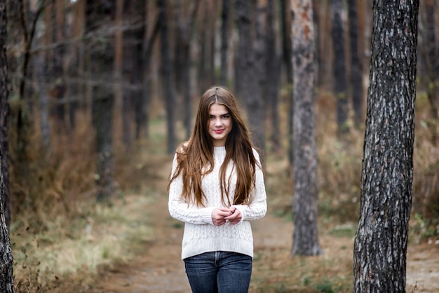 가을 숲에 서서 흰색 따뜻한 스웨터를 입은 아름다운 소녀의 초상
