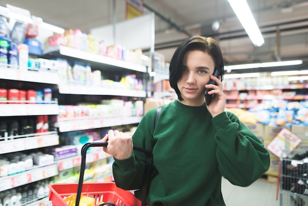 Портрет красивой девушки разговаривает по телефону во время покупок в супермаркете.