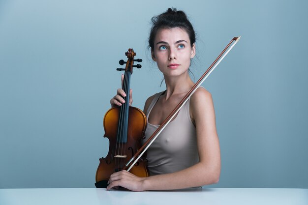 写真 青い背景の上に分離されたバイオリンとテーブルに座っている美しい若い女性の肖像画