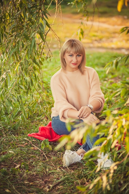 숲속의 공터에서 빨간 담요에 앉아 짧은 머리를 한 금발 여성의 초상화