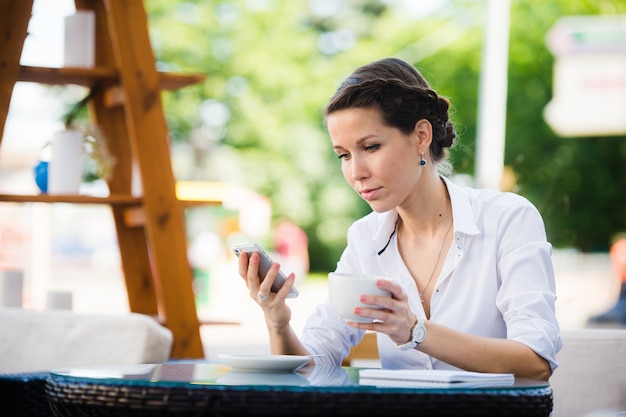 Портрет коммерсантки используя умный телефон в кафе тротуара.