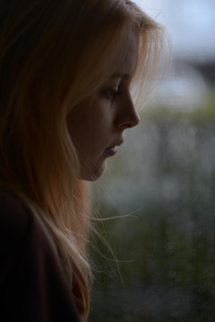 Фото Портрет девушки 18 лет с светлыми волосами возле окна в дождливый день
