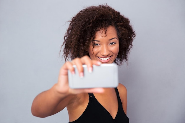 灰色の壁を越えてスマートフォンでselfie写真を作る幸せなアフリカ系アメリカ人女性の肖像画