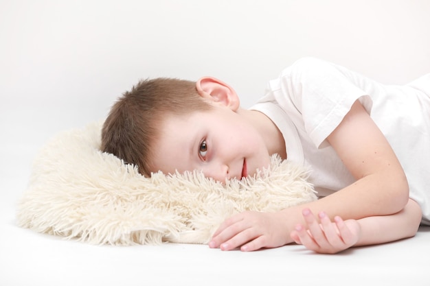 Фото Портрет счастливого милого маленького мальчика, просыпающегося утром и лежащего на белой подушке, изолированной на белом фоне. свежие и уютные простыни. перед сном для детей. концепция счастливого сновидения.