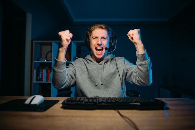 写真 自宅のテーブルに座ってゲームに勝つことを喜ぶ楽しいゲーマーの男の肖像画