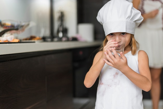 写真 ガラスの水を飲むシェフの帽子をかぶっているきれいな女の子の肖像画