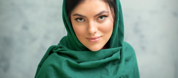 写真 灰色の背景に緑のヘッドスカーフで化粧をしたかなり若い白人女性の肖像画。