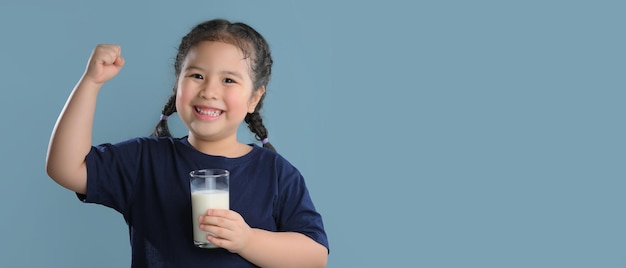 Фото Портрет довольной милой маленькой девочки со стаканом молока на синем фоне.