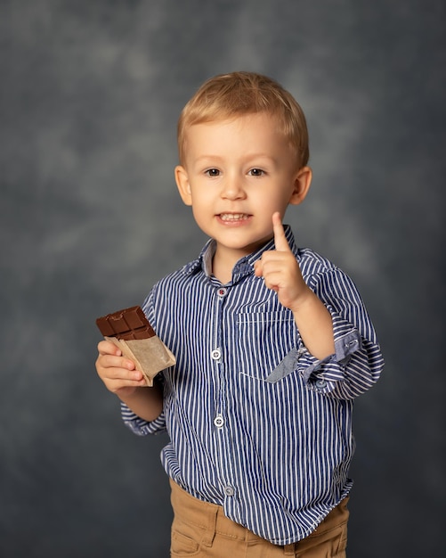 写真 灰色の背景にチョコレートを食べている小さな男の子の肖像画 幸せな子供時代のコンセプト 甘い歯