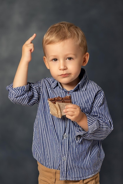 写真 灰色の背景にチョコレートを食べている小さな男の子の肖像画 幸せな子供時代のコンセプト 甘い歯