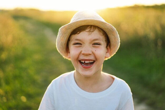 사진 하 티셔츠와 모자를 입고 웃는 작은 소년의 초상화가 해가 지는 동안 야외에서 놀고 있습니다.