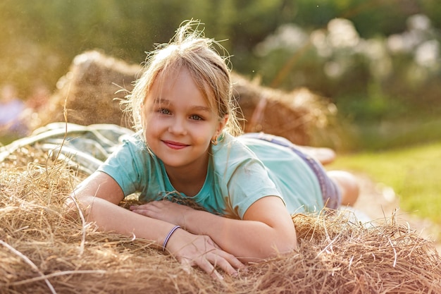 写真 干し草の山の幸せな子供時代の暑い夏の夜に横たわっている笑顔の歳のブロンドの女の子の肖像画