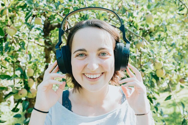 写真 公園のカメラに微笑んでいるヘッドフォンで若い遊び心のある流行に敏感なアメリカ人女性の肖像画。屋外