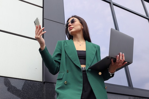 Фото Портрет молодой женщины в деловом костюме с ноутбуком и мобильным телефоном