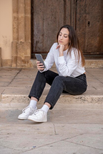 写真 携帯電話から読んで座っている若い女性の肖像画